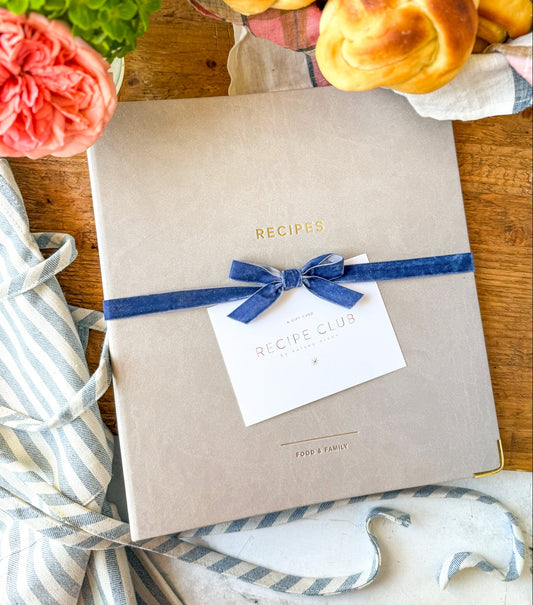 Recipe Binder with a blue ribbon on a wooden table with flowers and bread.